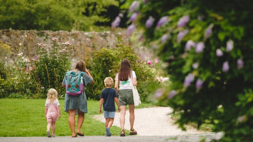 A family with two adults and two children walk towards the rose garden at Buckland Abbey.